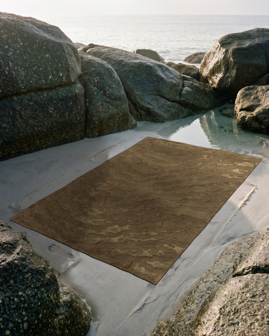 Tapis Gerald moiré vert olive posé sur le sable entre les rochers de granit à marée basse, tufté main laine et Tencel Rugier