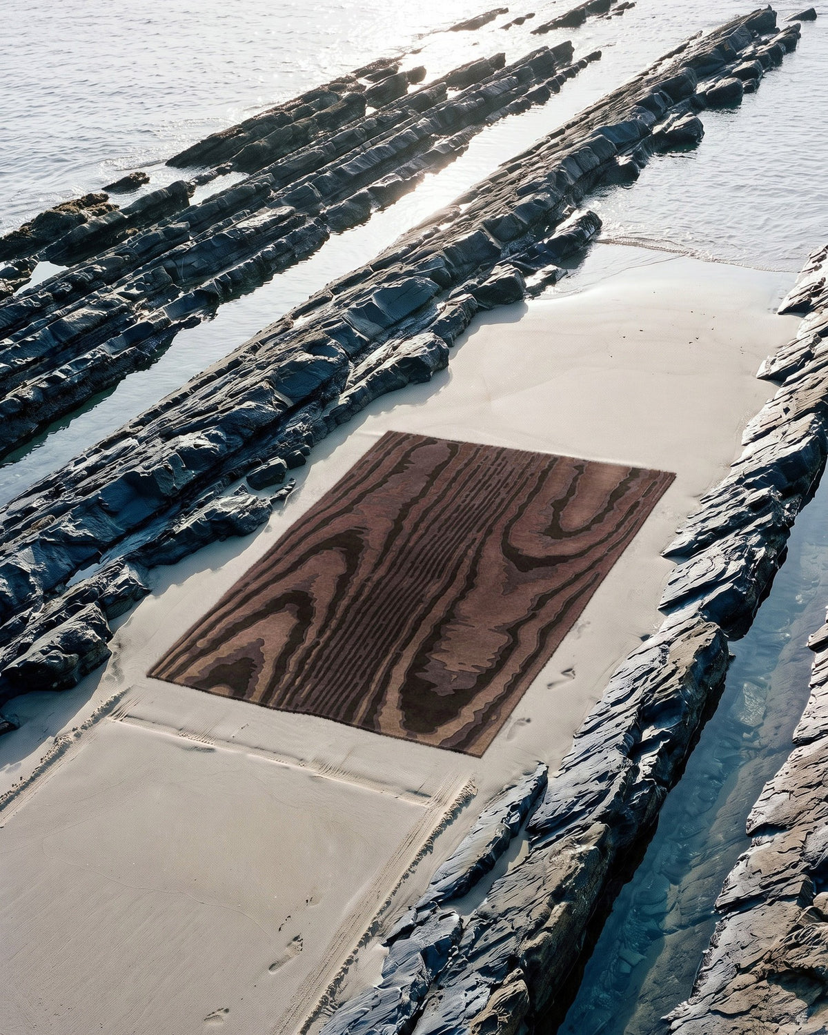 Tapis Harlan moiré brun posé sur une bande de sable entre les rochers de schiste à marée basse, tufté main laine et Tencel Rugier
